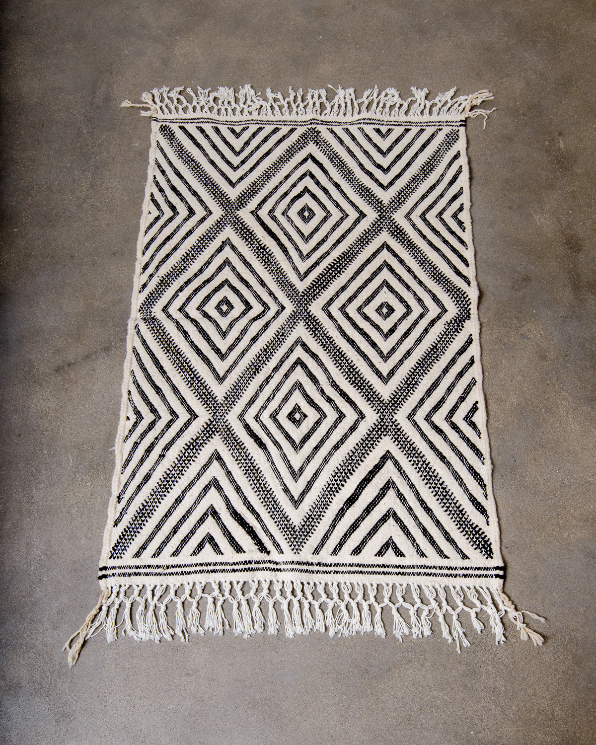 Small Kelim Rug in black and cream laying on concrete studio floor.